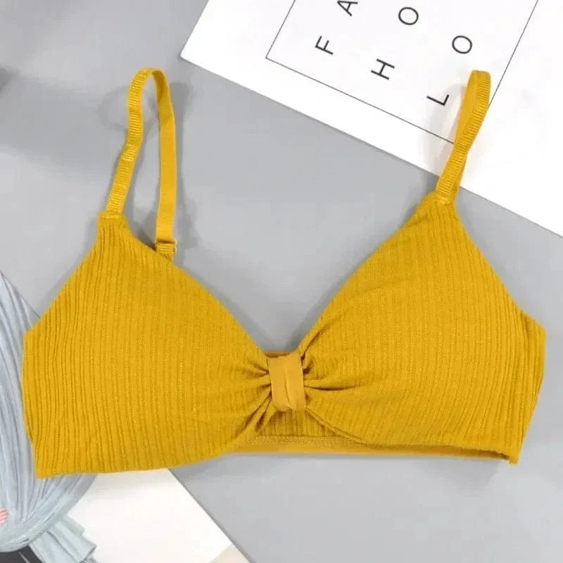 A mustard yellow ribbed bralette with adjustable straps and a central knotted detail resting on a light grey surface.