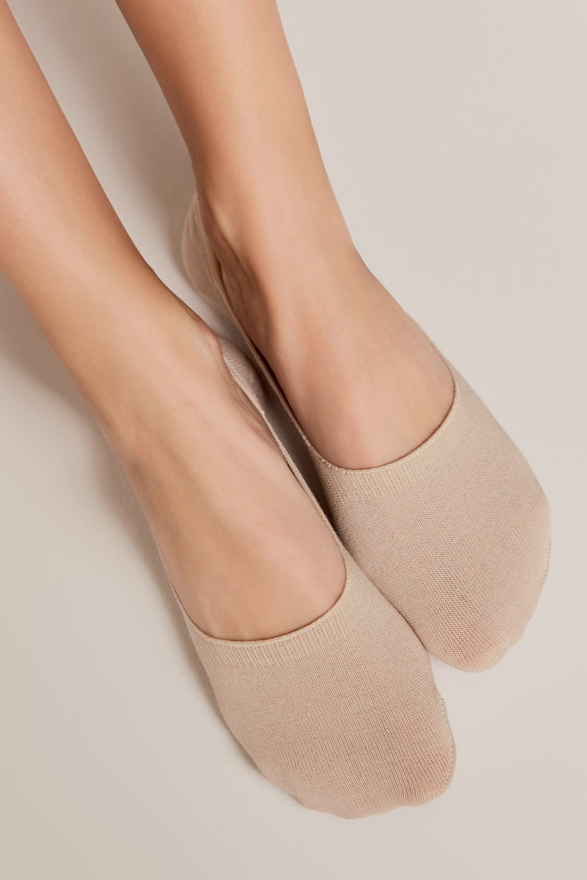 A pair of nude-colored, low-cut liner socks worn on feet against a light background.