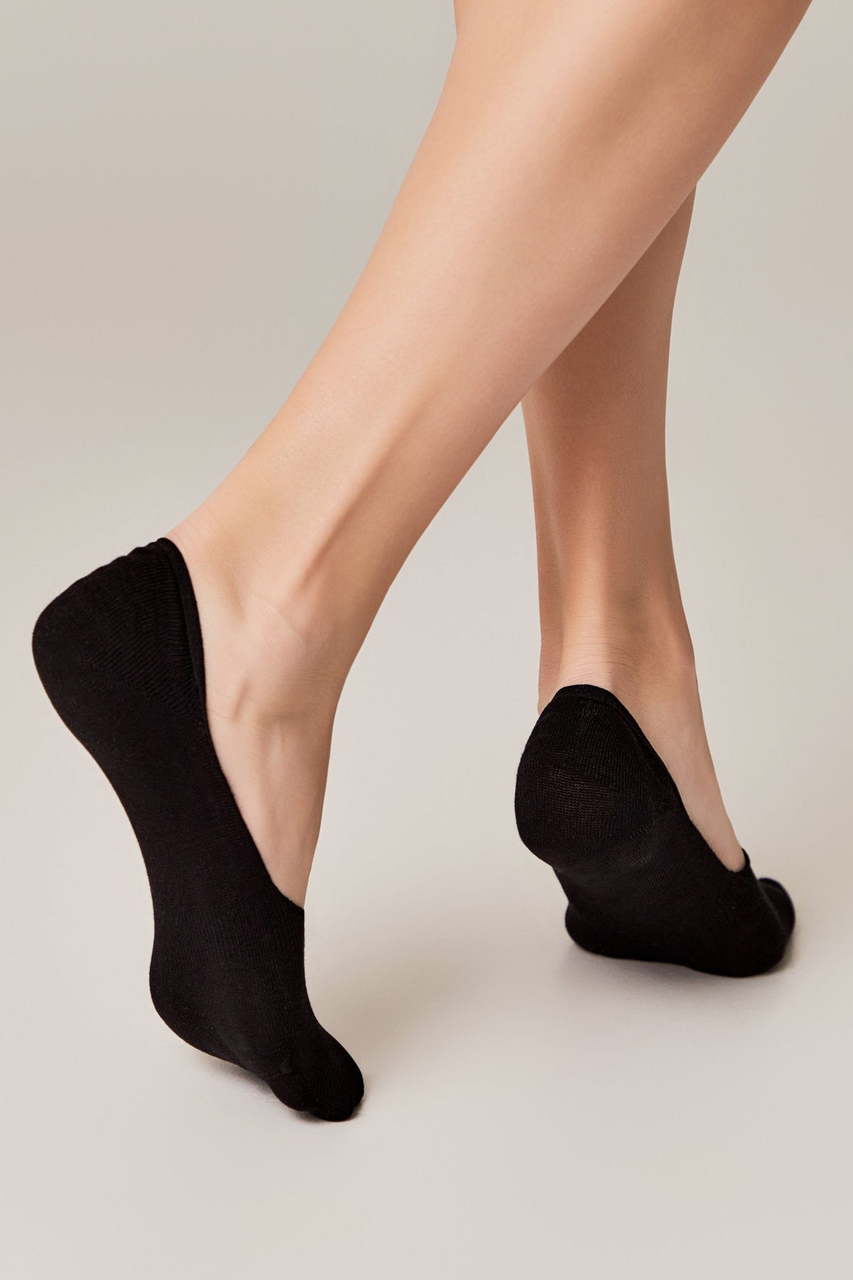 A pair of black low-cut no-show socks worn on a person's feet against a plain light grey background.