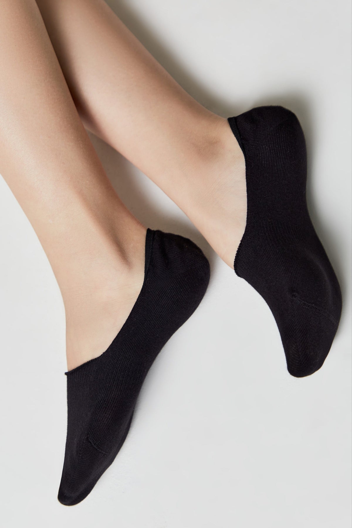 A pair of black low-cut no-show socks worn on a person's feet against a plain white background.