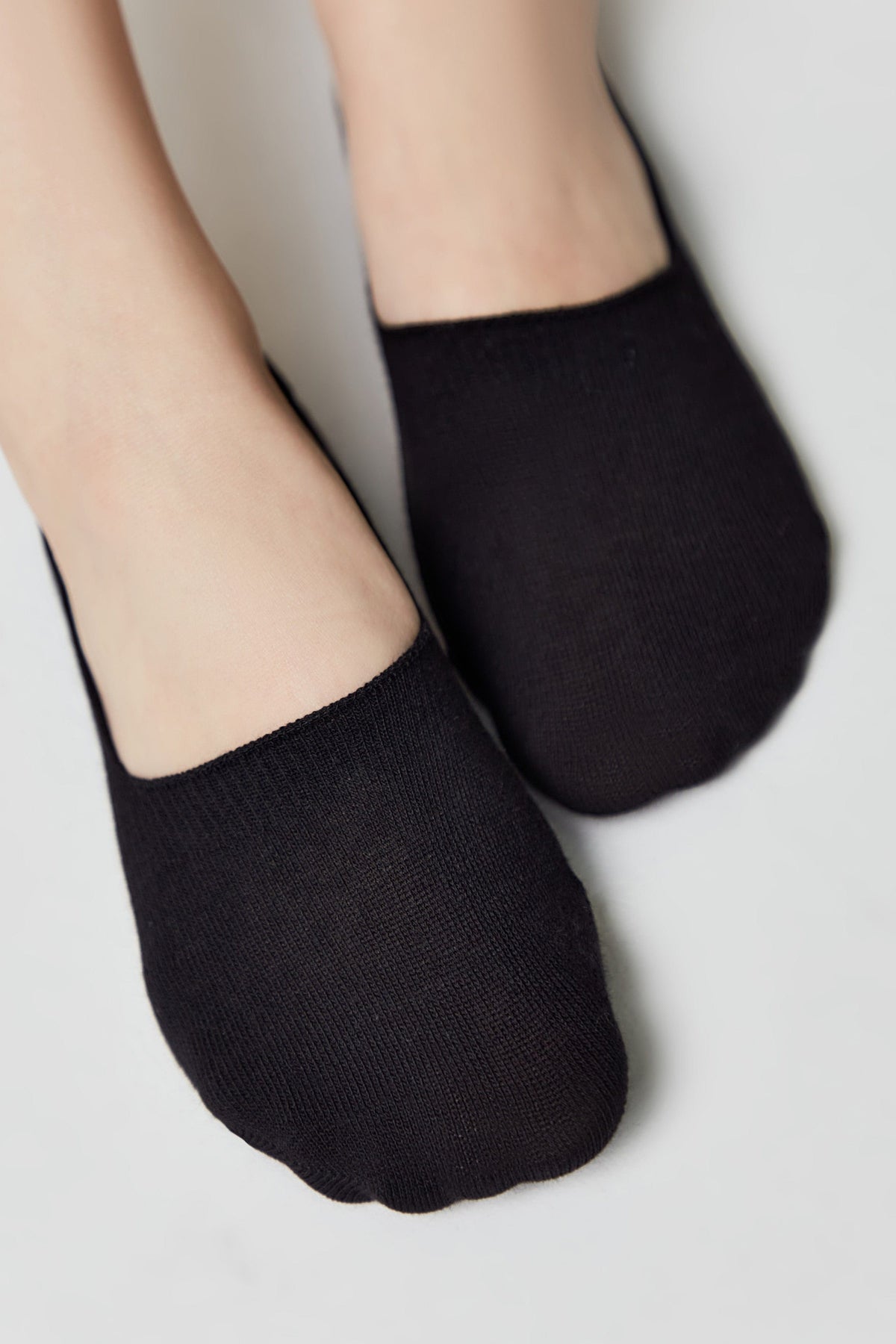 A pair of black low-cut, no-show socks worn on feet against a plain white background.