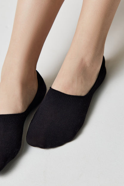A pair of black no-show socks worn on a person's feet against a plain white background.