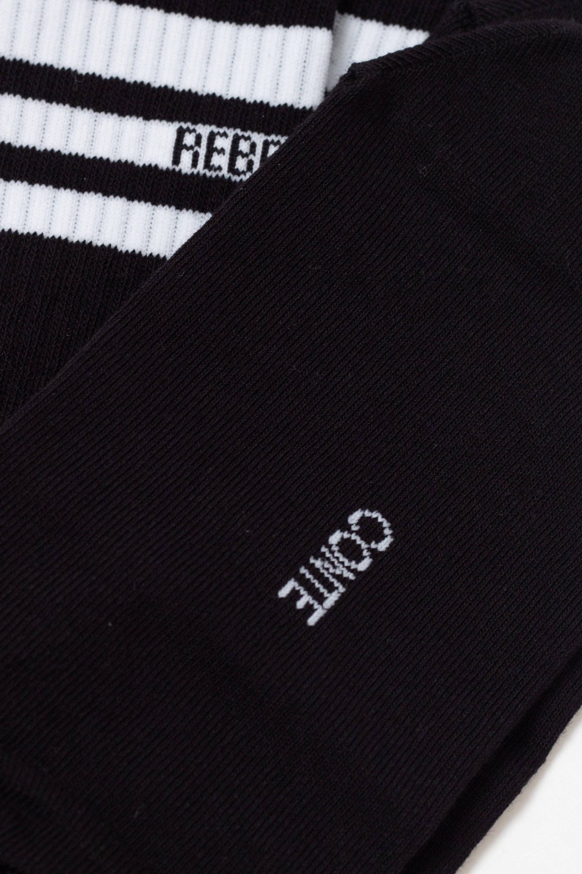 A close-up of a pair of black socks features a white logo with the text CONTE on one side and a ribbed top section with white stripes and partial lettering on the other.