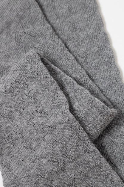A close-up view of grey, pointelle-knit fabric with a delicate, repeating diamond-shaped lace pattern folded over itself against a white background.