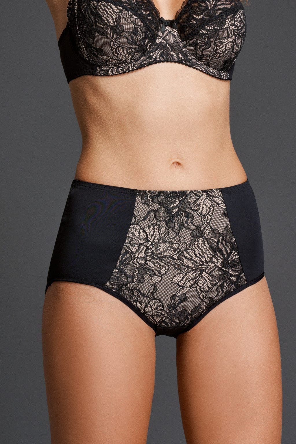 A model wearing high-waisted black briefs featuring a beige-lined floral lace panel at the front.
