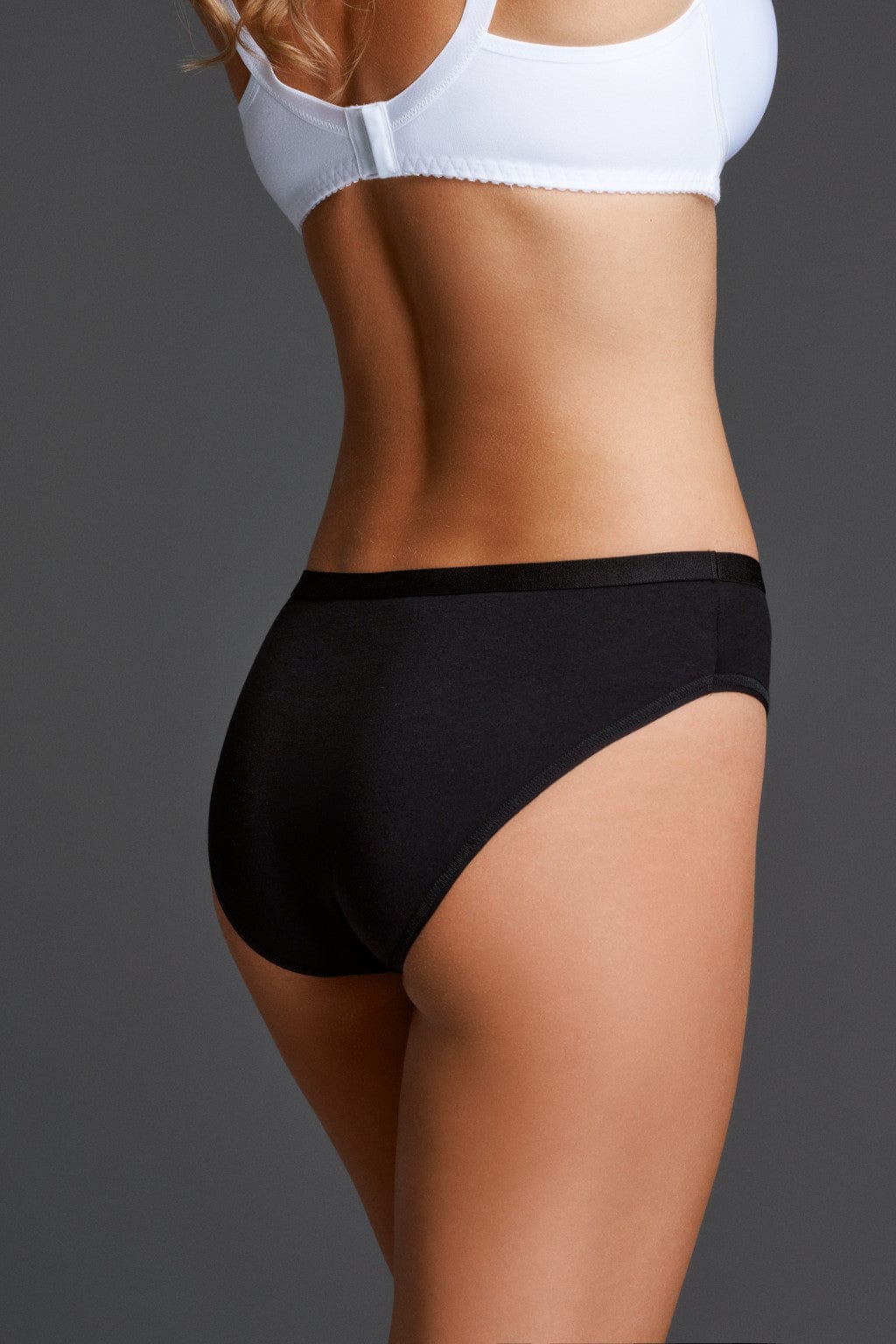 Black bikini-style panties with a wide elastic waistband worn on a model against a grey background.