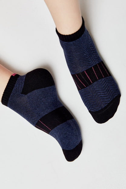 A pair of ankle socks with a dark blue and black geometric chevron pattern and thin pink accent lines worn on feet.