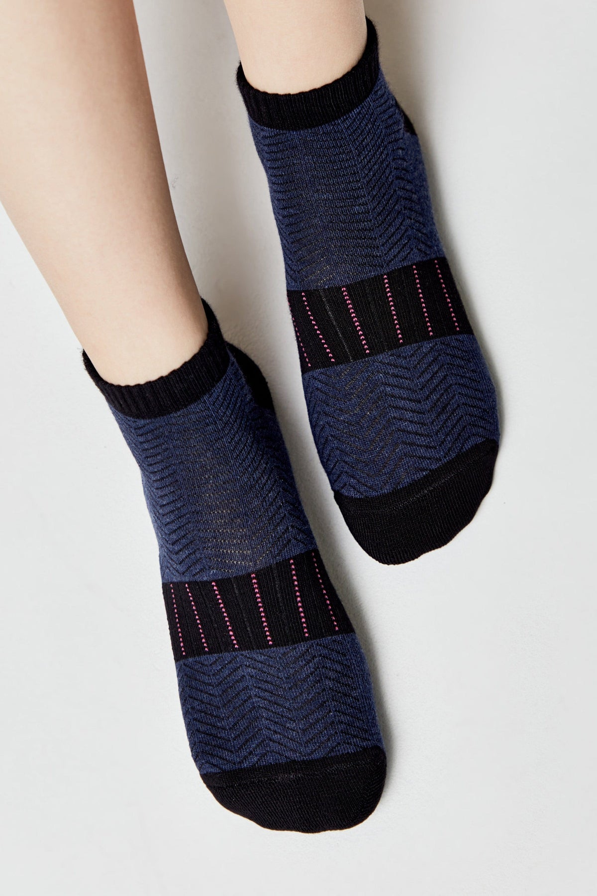 A pair of ankle-length socks featuring a dark blue herringbone knit pattern, a black toe and cuff, and a horizontal band across the foot with thin vertical pink stripes.
