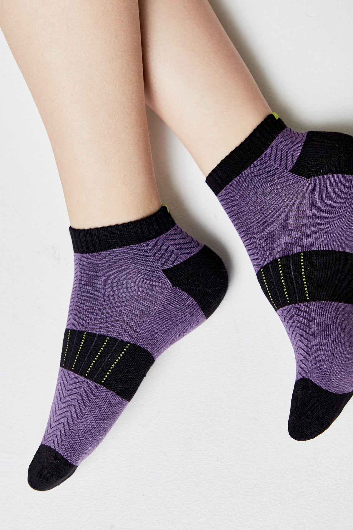 Ankle socks featuring a purple and black geometric chevron pattern with solid black toe, heel, and cuff accents, shown on a person's feet against a plain white background.