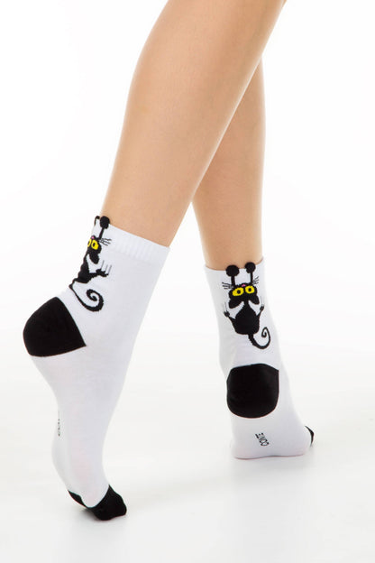 A pair of white ankle socks worn on legs, each featuring a cartoon black cat with large yellow eyes on the outer side and contrasting black heel and toe panels.