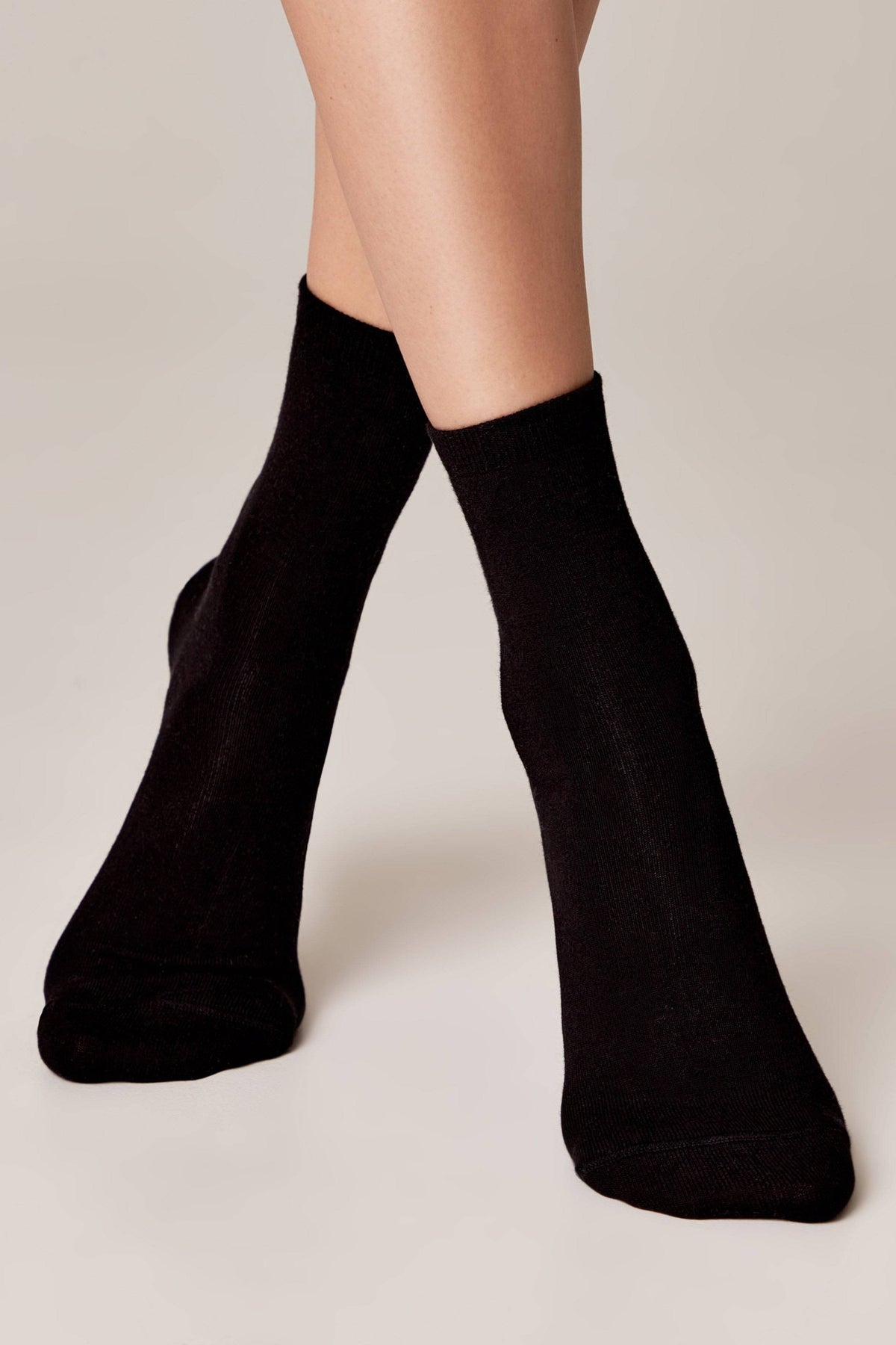 A pair of solid black mid-calf crew socks worn on a person's feet against a light neutral background.