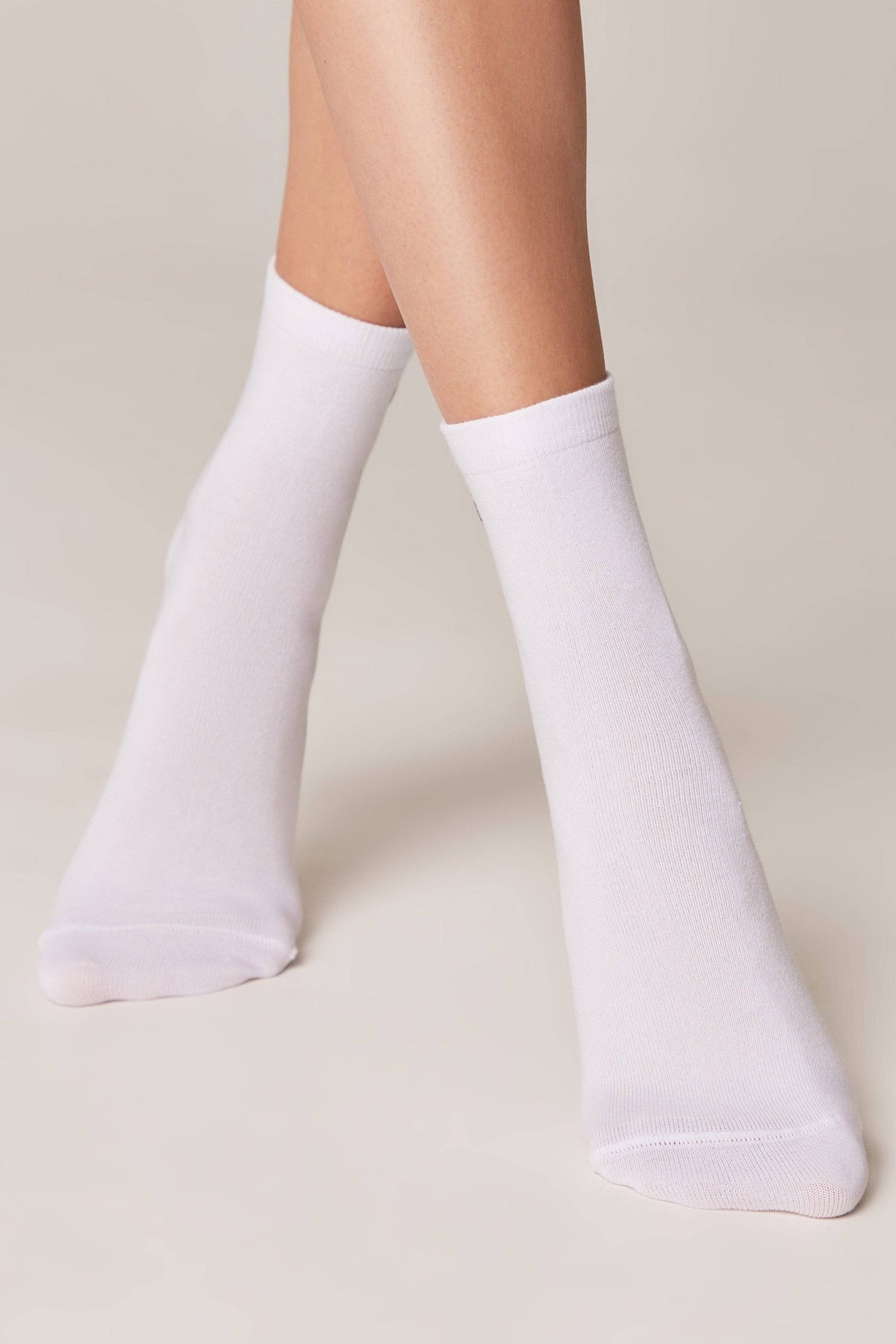 A pair of plain white crew socks worn on a person's feet against a neutral background.