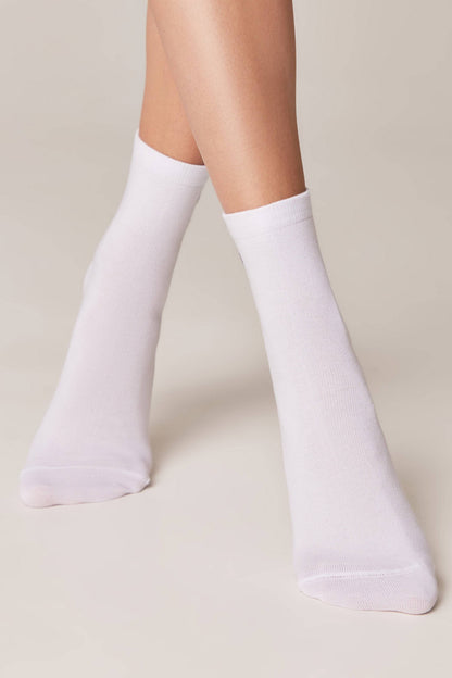 A pair of plain white crew socks worn on a person's feet against a neutral background.