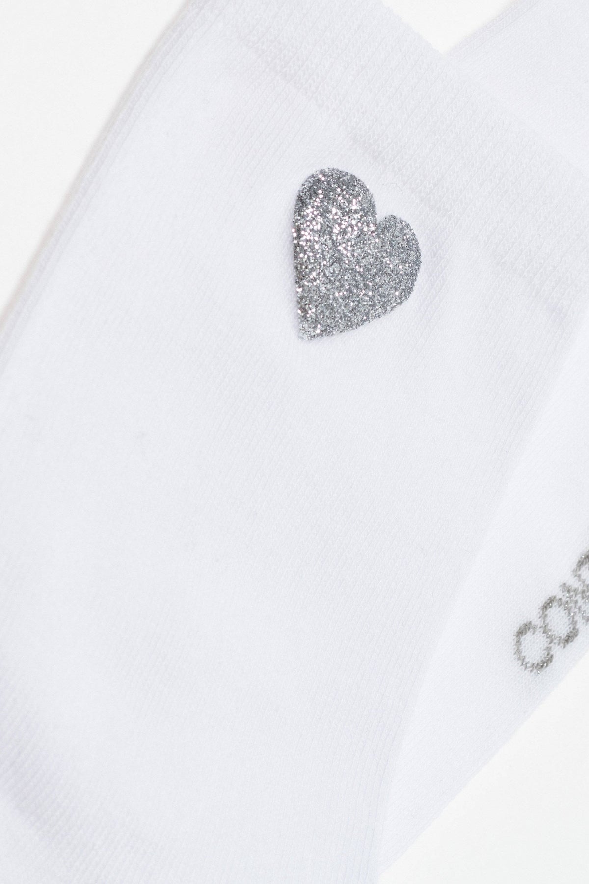 A white sock featuring a silver glitter heart embellishment on the side.