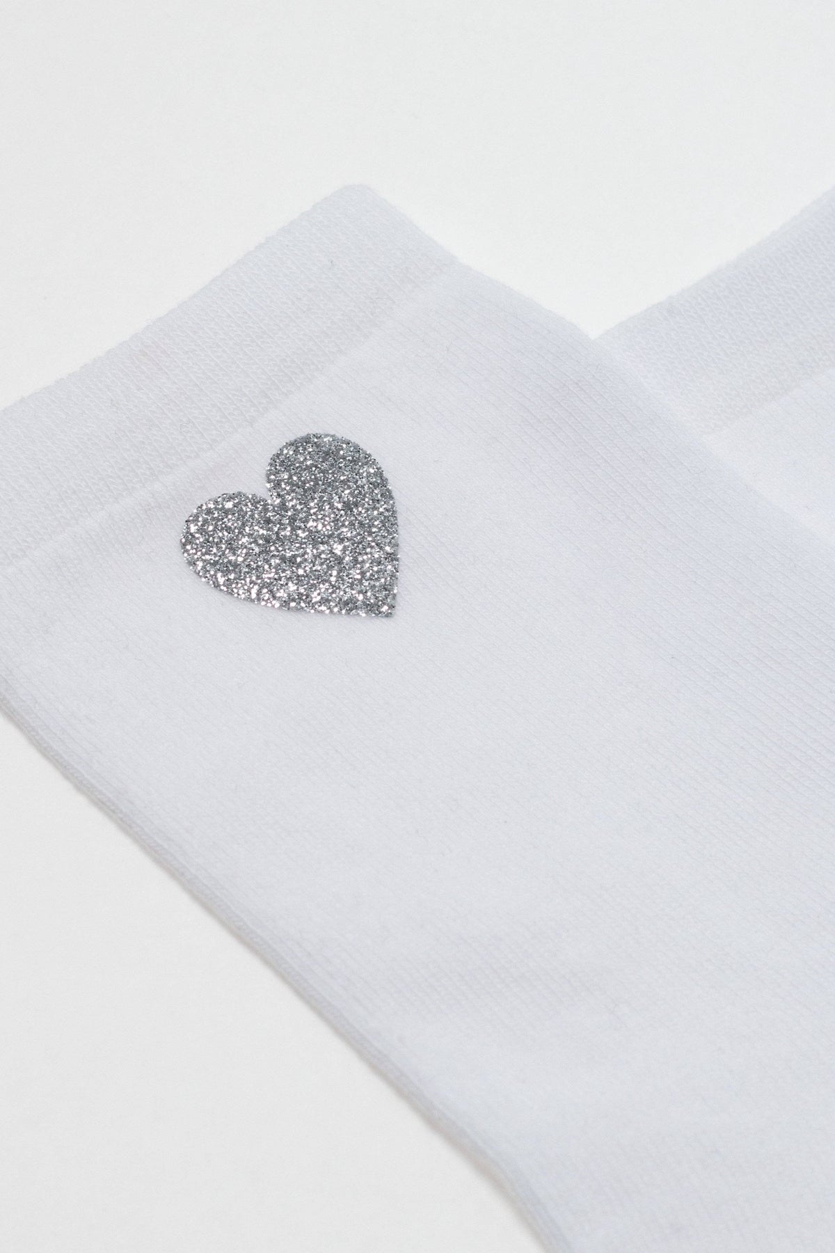 A white sock featuring a silver glitter heart accent on the side.