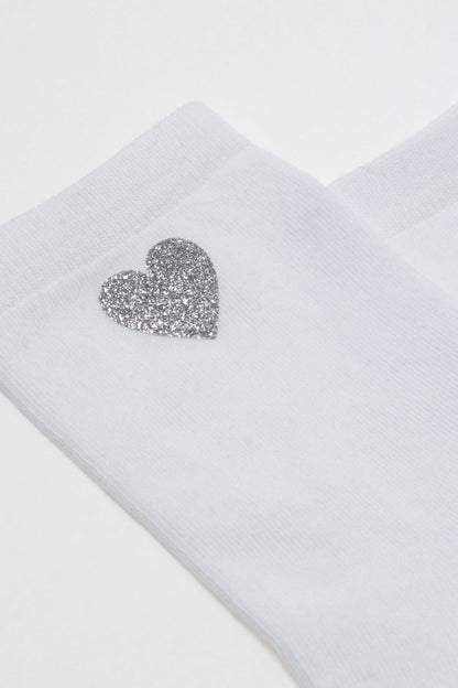 A white sock featuring a silver glitter heart accent on the side.