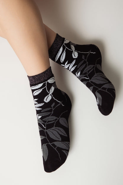 Ankle socks featuring a black and gray leafy botanical pattern with a subtle glittery trim at the cuff, worn on a person's feet against a plain light background.
