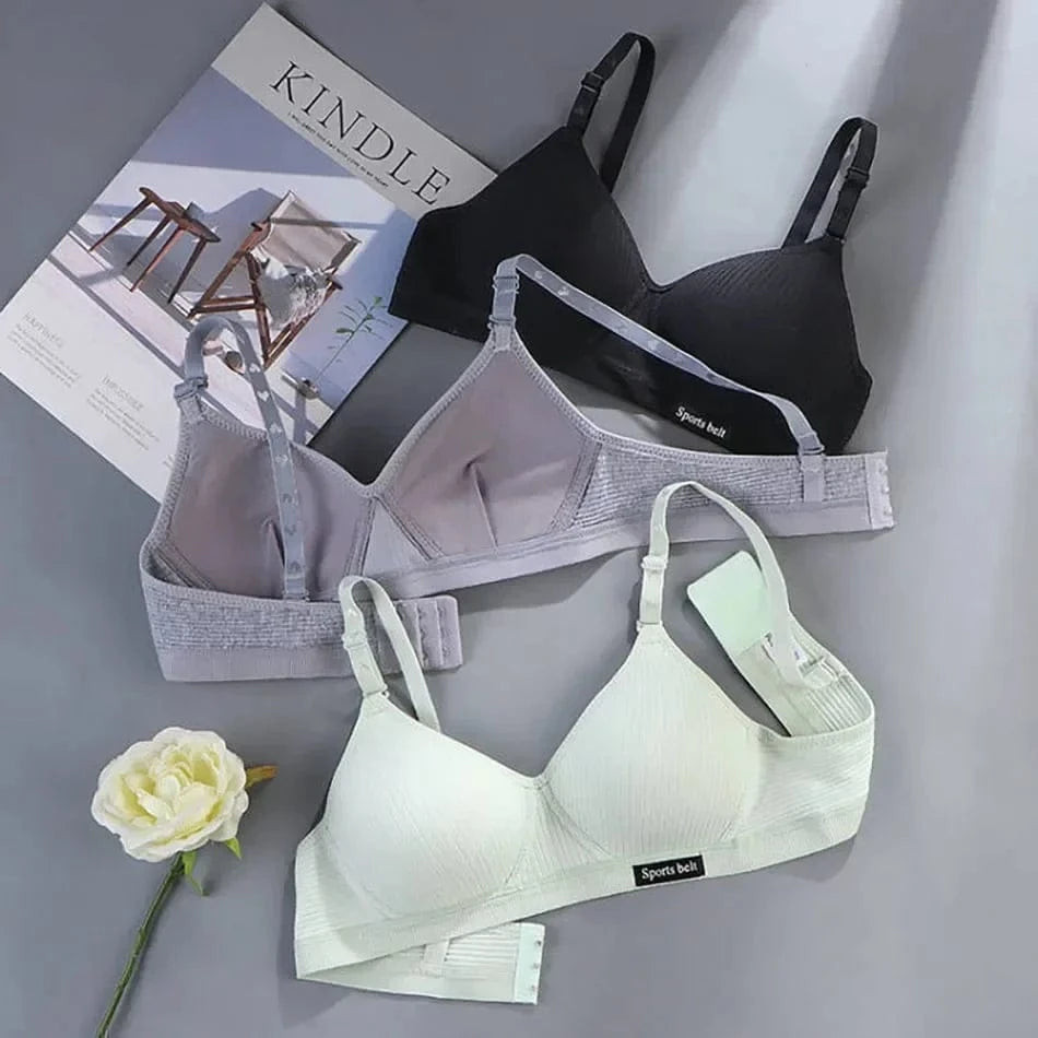 Three wireless bras in black, gray, and light green are laid out on a gray surface next to a white rose and a Kindle catalog.