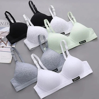 Seven sports bras in various shades of white, grey, black, and light green are arranged on a grey surface, each featuring adjustable straps and a small Sports belt label.