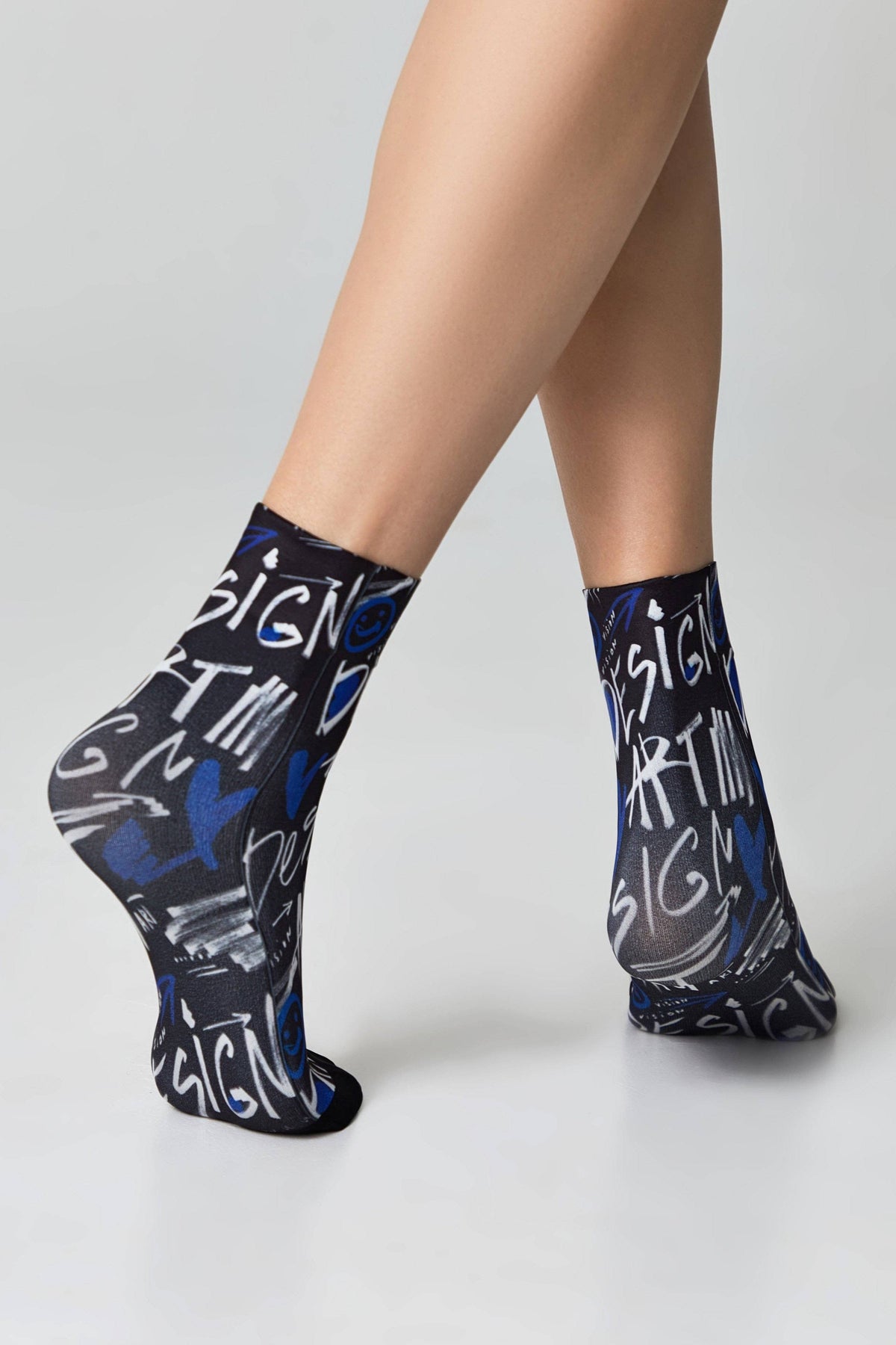 A pair of black ankle socks featuring a white and blue graffiti-style graphic pattern of words and shapes worn on a person's feet.