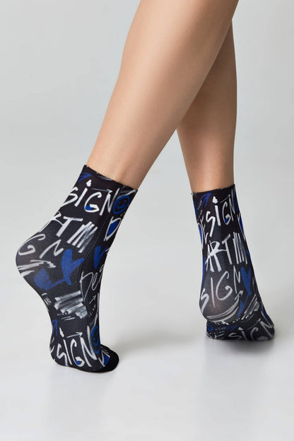 A pair of black ankle socks featuring a white and blue graffiti-style graphic pattern of words and shapes worn on a person's feet.