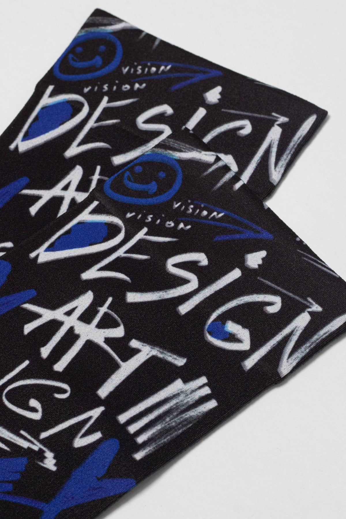 A pair of black socks featuring an all-over white and blue graffiti-style print with the words DESIGN, ART, and VISION alongside blue smiley face icons.