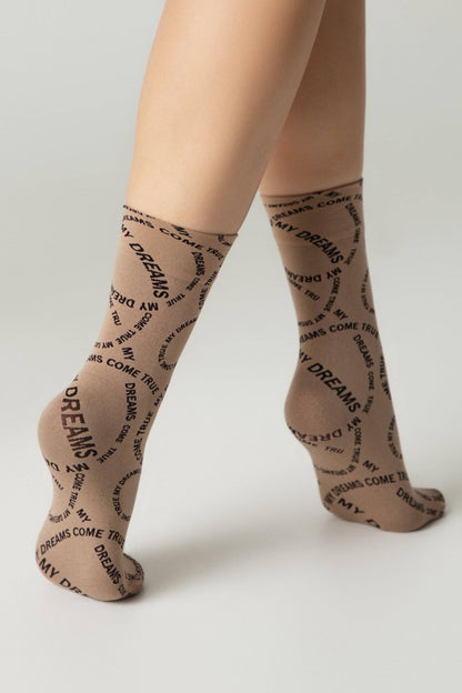 Tan socks featuring a repeating black print of the phrase MY DREAMS COME TRUE are worn on a person's feet against a neutral background.