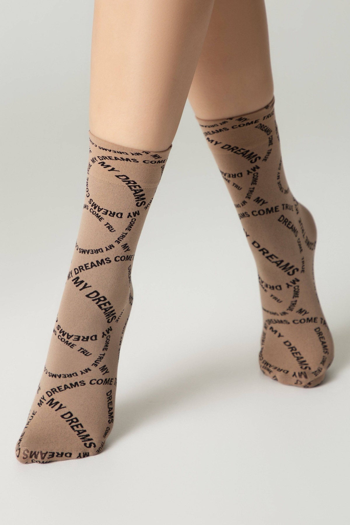 Tan crew-length socks with the repeating black text "MY DREAMS COME TRUE" worn on a person's legs against a neutral background.