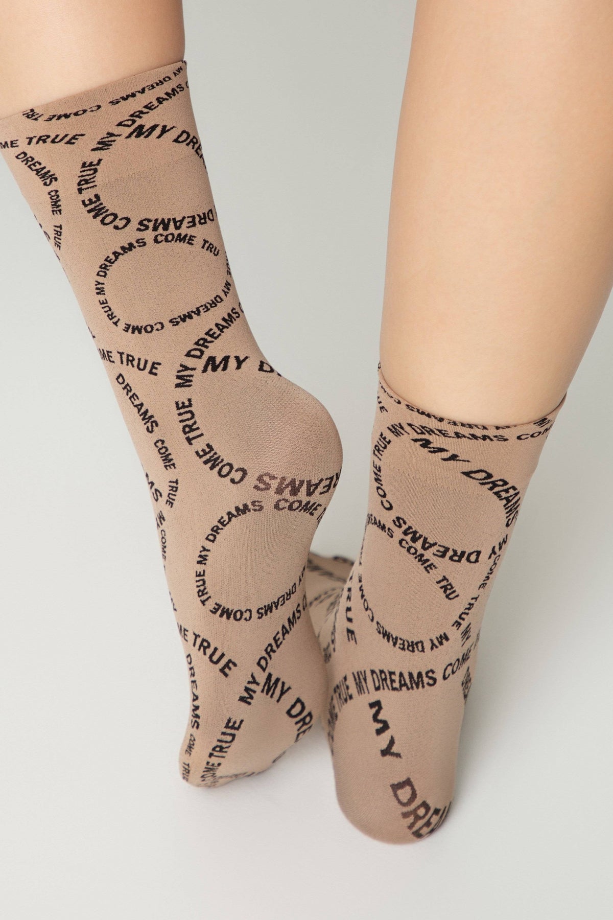 A pair of tan-colored socks featuring a repetitive pattern of the words 'MY DREAMS COME TRUE' in black text.