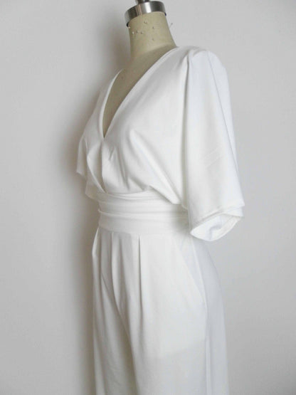 A white V-neck jumpsuit with wide sleeves and a fitted waistband displayed on a mannequin against a plain white background.