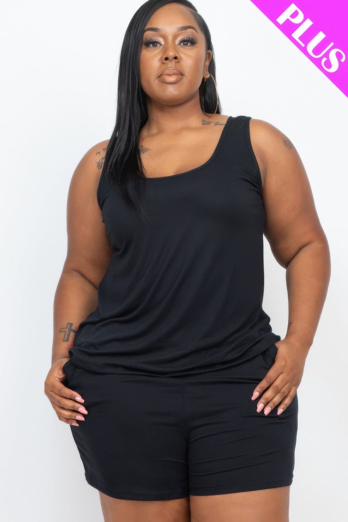 A woman with long black hair wearing a simple black sleeveless tank top paired with matching black shorts, positioned against a white studio background.
