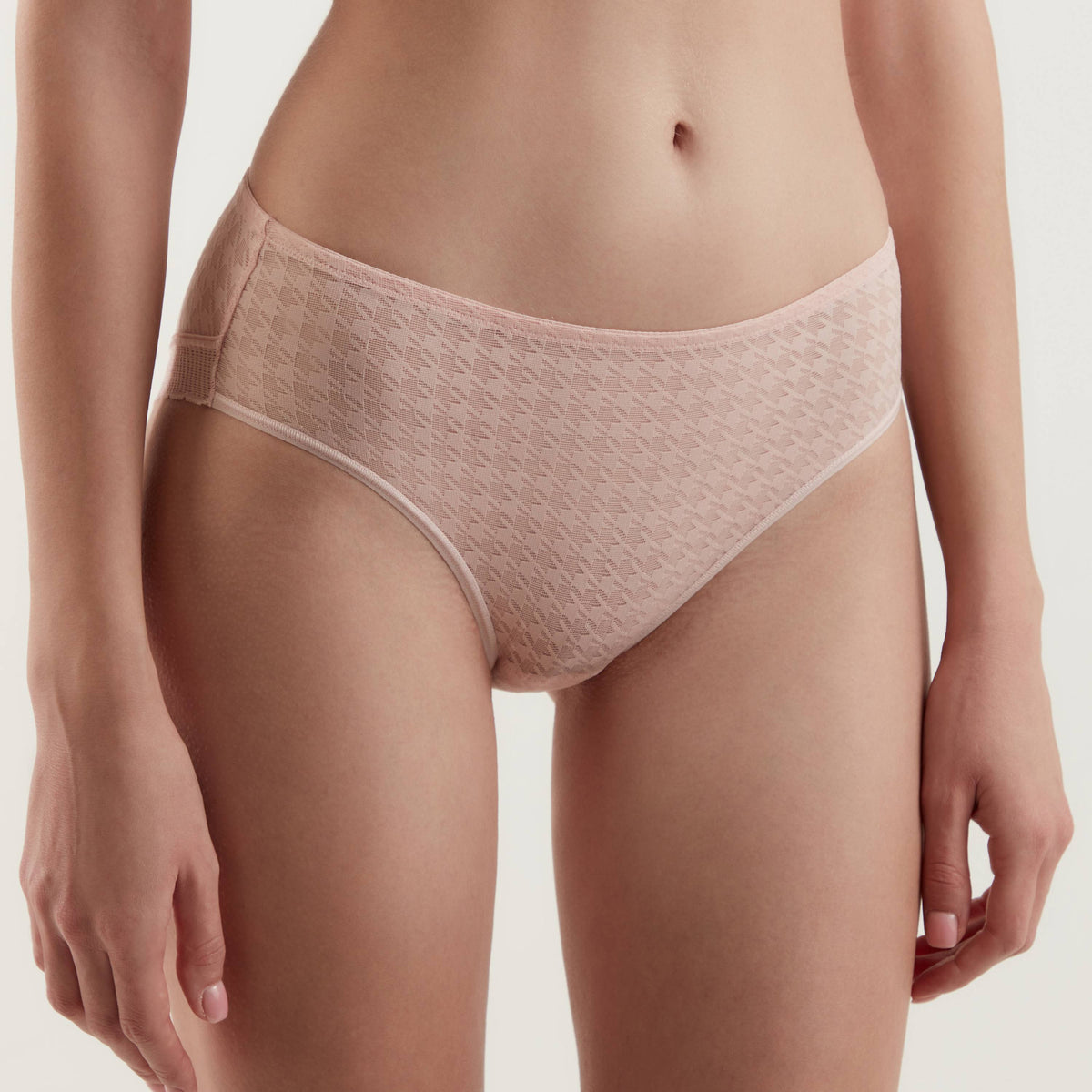 A pair of light pink, low-rise bikini briefs with a subtle houndstooth texture, worn by a person against a neutral background.