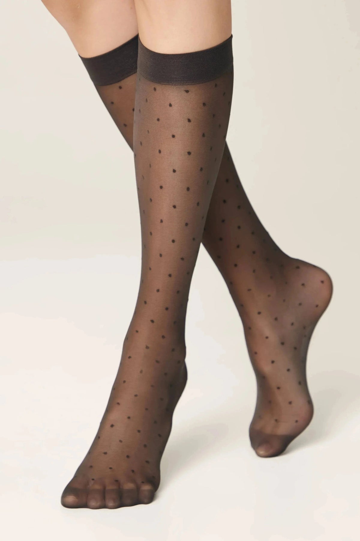 Sheer black knee-high stockings with small polka dot patterns worn on a person's legs against a light background.
