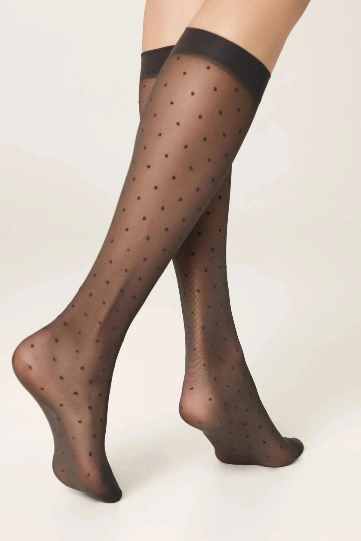 Sheer black knee-high stockings featuring a small repeating polka dot pattern against a plain off-white background.
