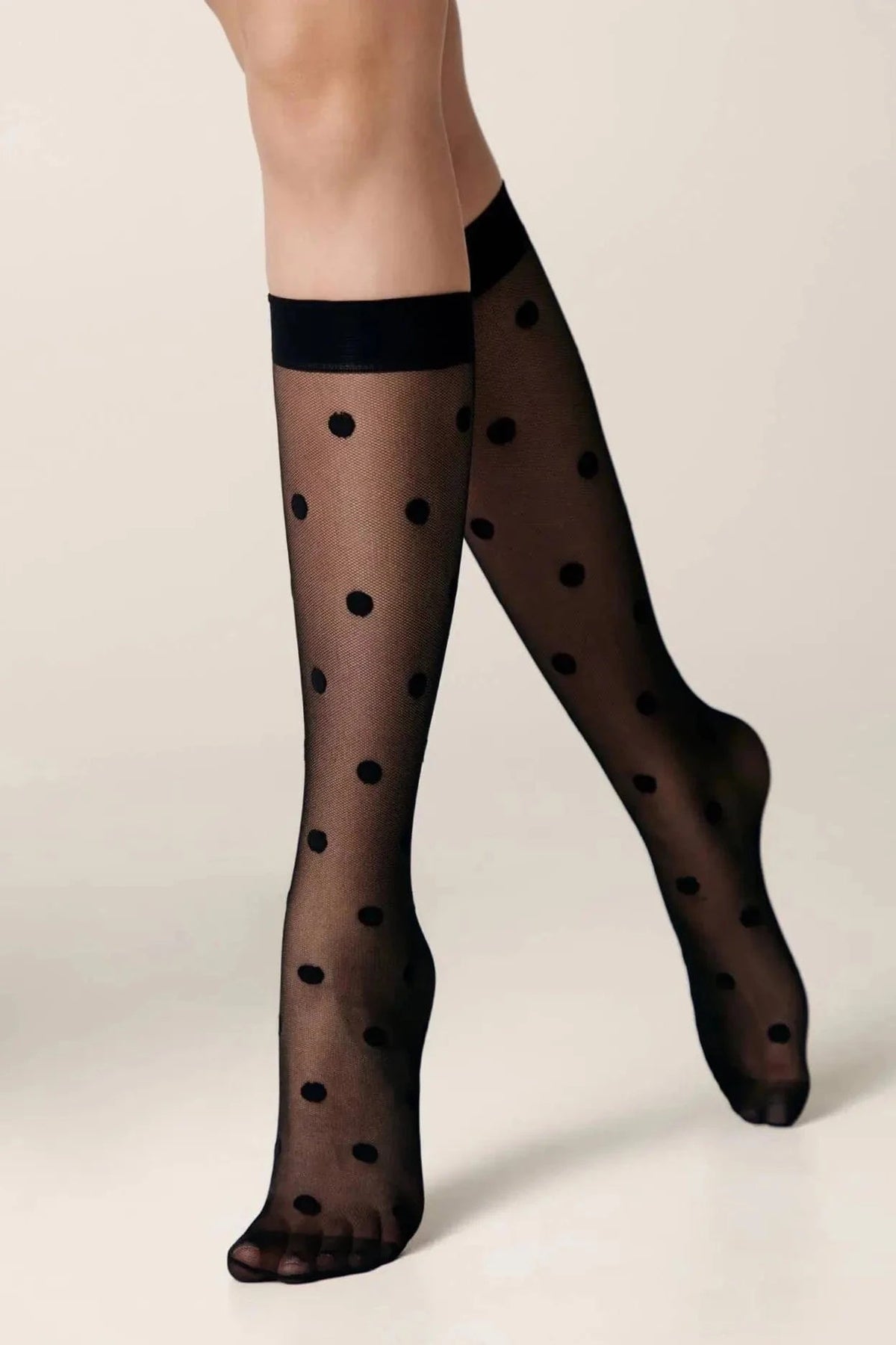 Sheer black knee-high stockings patterned with small black polka dots on a light neutral background.