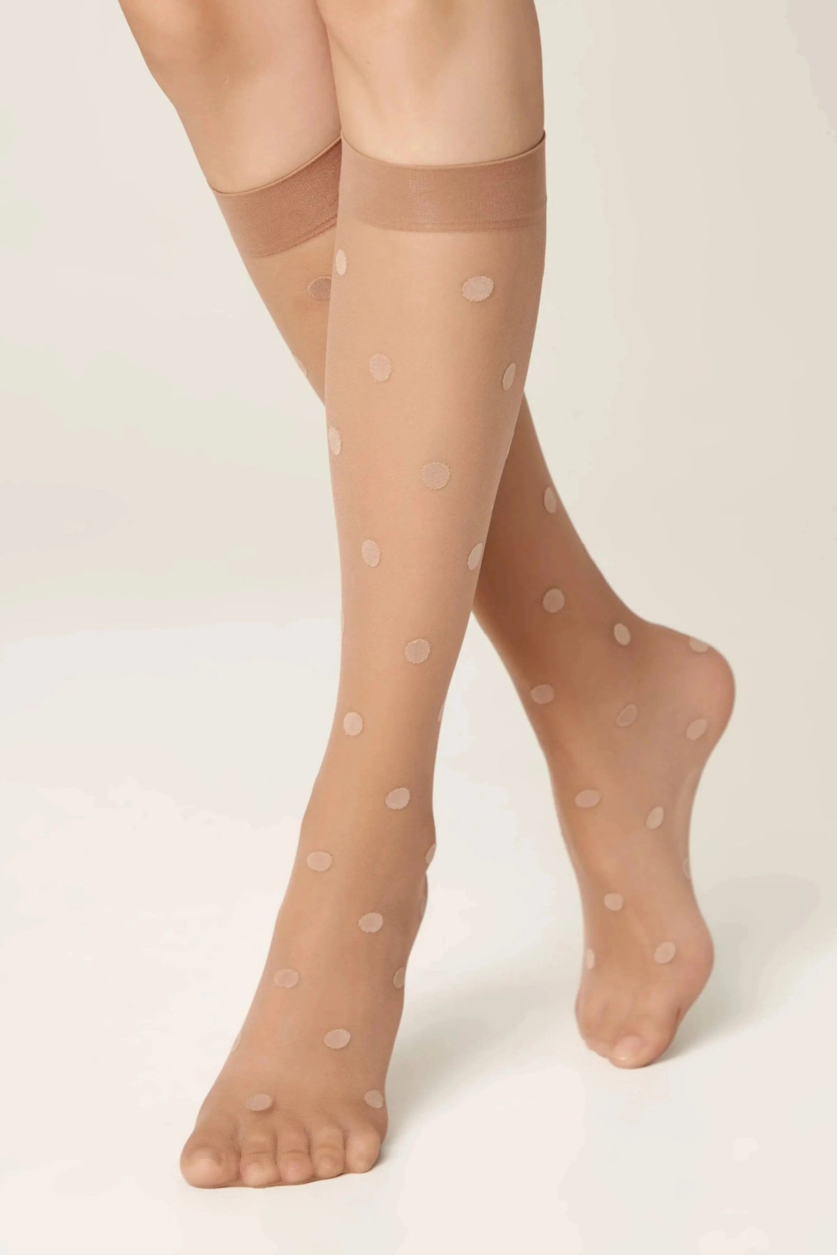 Sheer beige knee-high stockings featuring a subtle polka dot pattern worn on a person's legs against a neutral background.