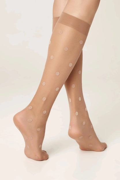 Sheer beige knee-high stockings featuring a repeating pattern of light-colored polka dots worn on a pair of legs.