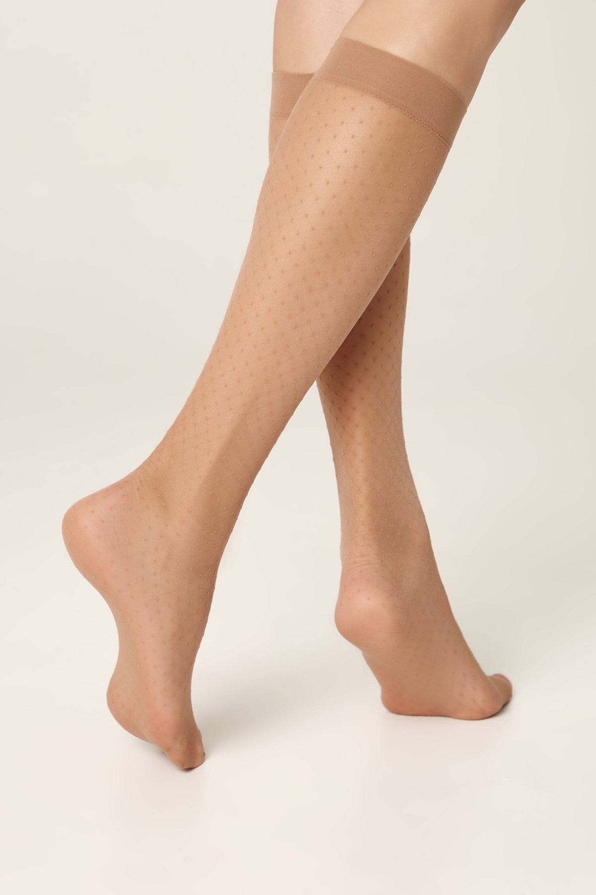 Sheer nude knee-high stockings featuring a delicate tonal dot pattern worn on a person's legs against a plain light background.