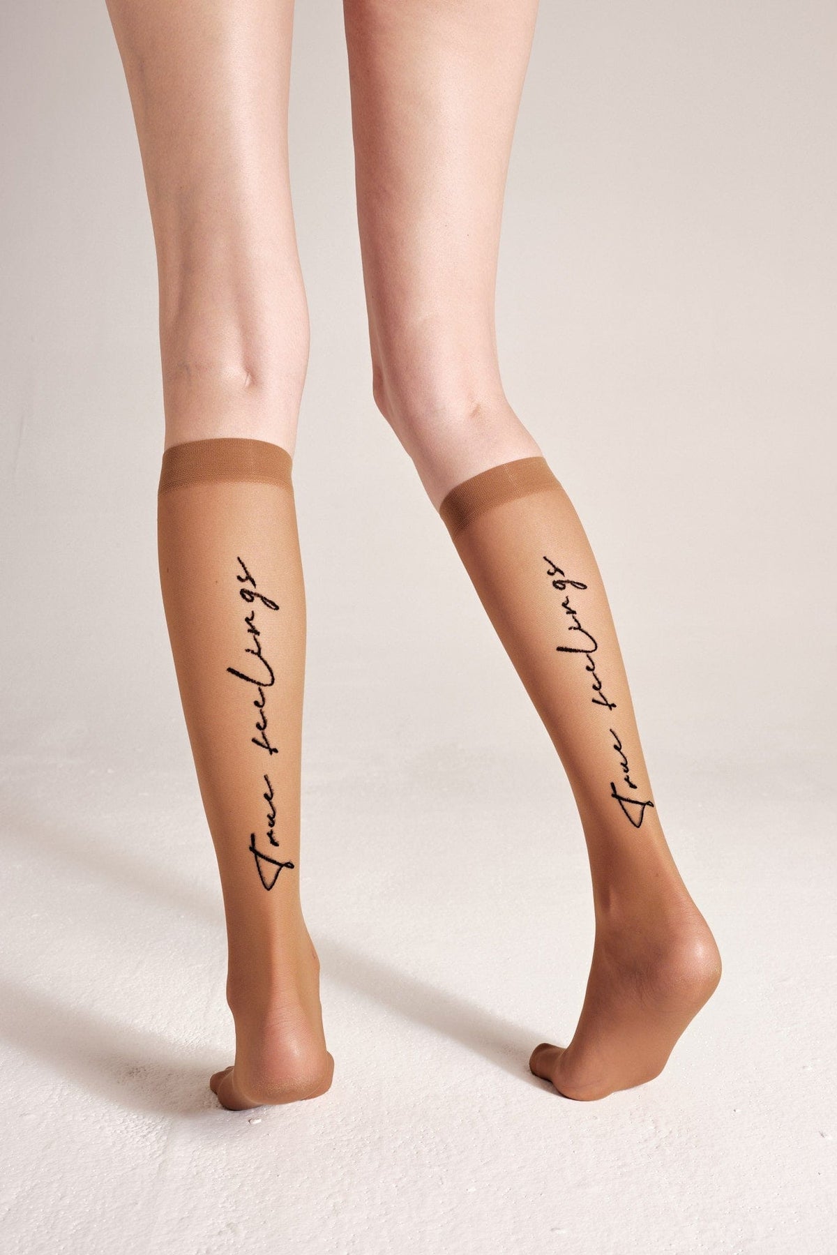 Sheer tan knee-high socks featuring the words true feelings printed in black script on the back of each leg.