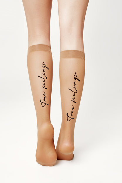 A pair of sheer beige knee-high stockings worn on the lower legs, featuring the words true feelings written in a cursive black font down the back of each calf.