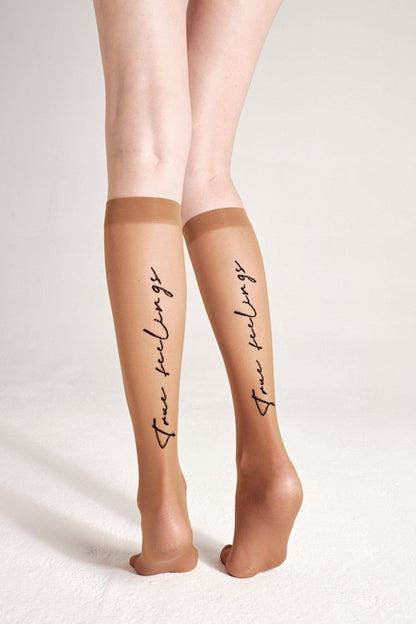 Sheer tan knee-high stockings worn on a person's legs, featuring the black cursive script words true feelings printed vertically on the back of each calf.