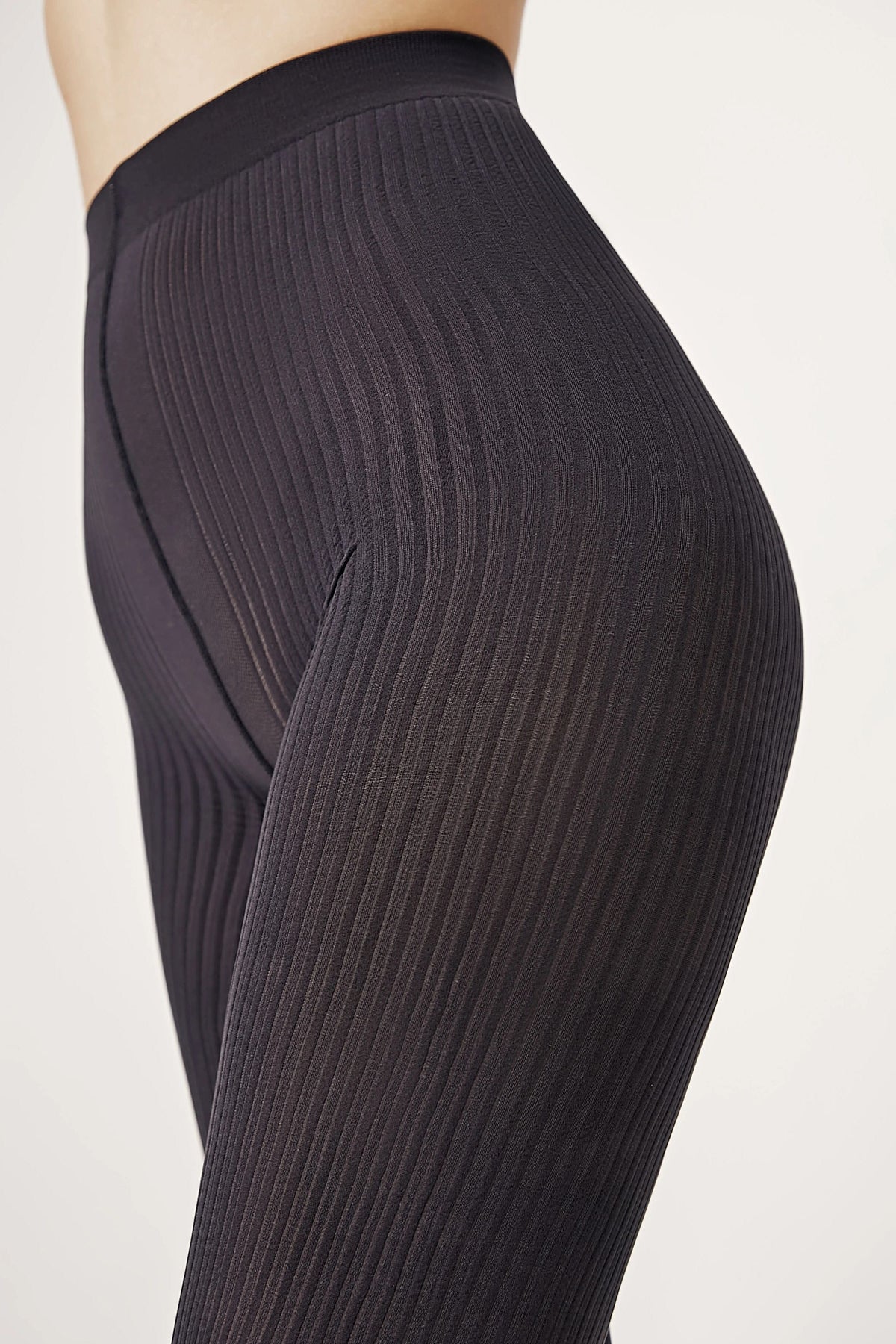 A close-up view of black, vertically ribbed leggings worn on a person, highlighting the textured fabric and high-waisted fit.