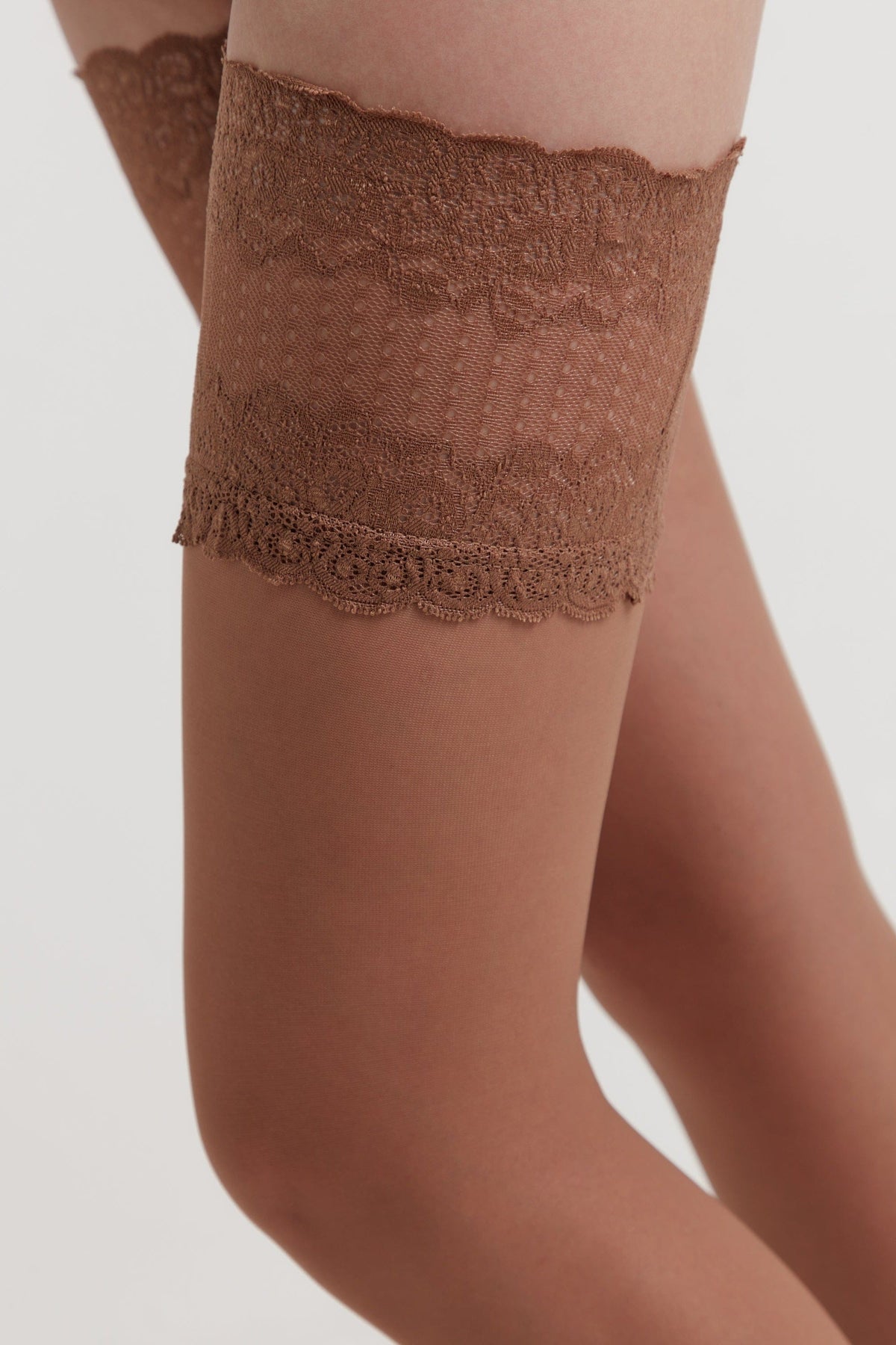 A close-up of a leg wearing sheer tan hosiery topped with a wide band of intricate, brown floral lace.