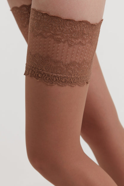A close-up of a leg wearing sheer tan hosiery topped with a wide band of intricate, brown floral lace.