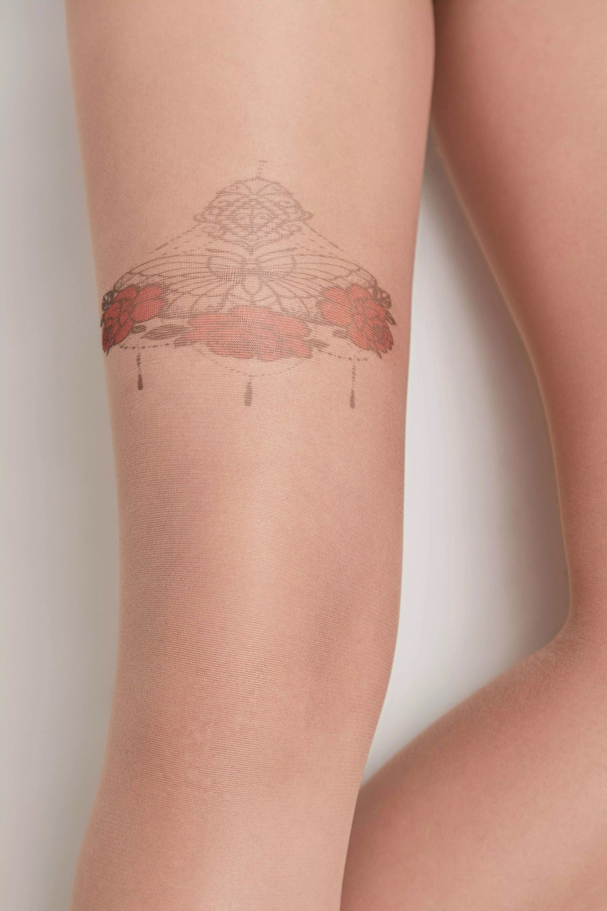 Nude sheer tights featuring a delicate black lace-inspired geometric tattoo design on the thigh, accented with small red floral details.