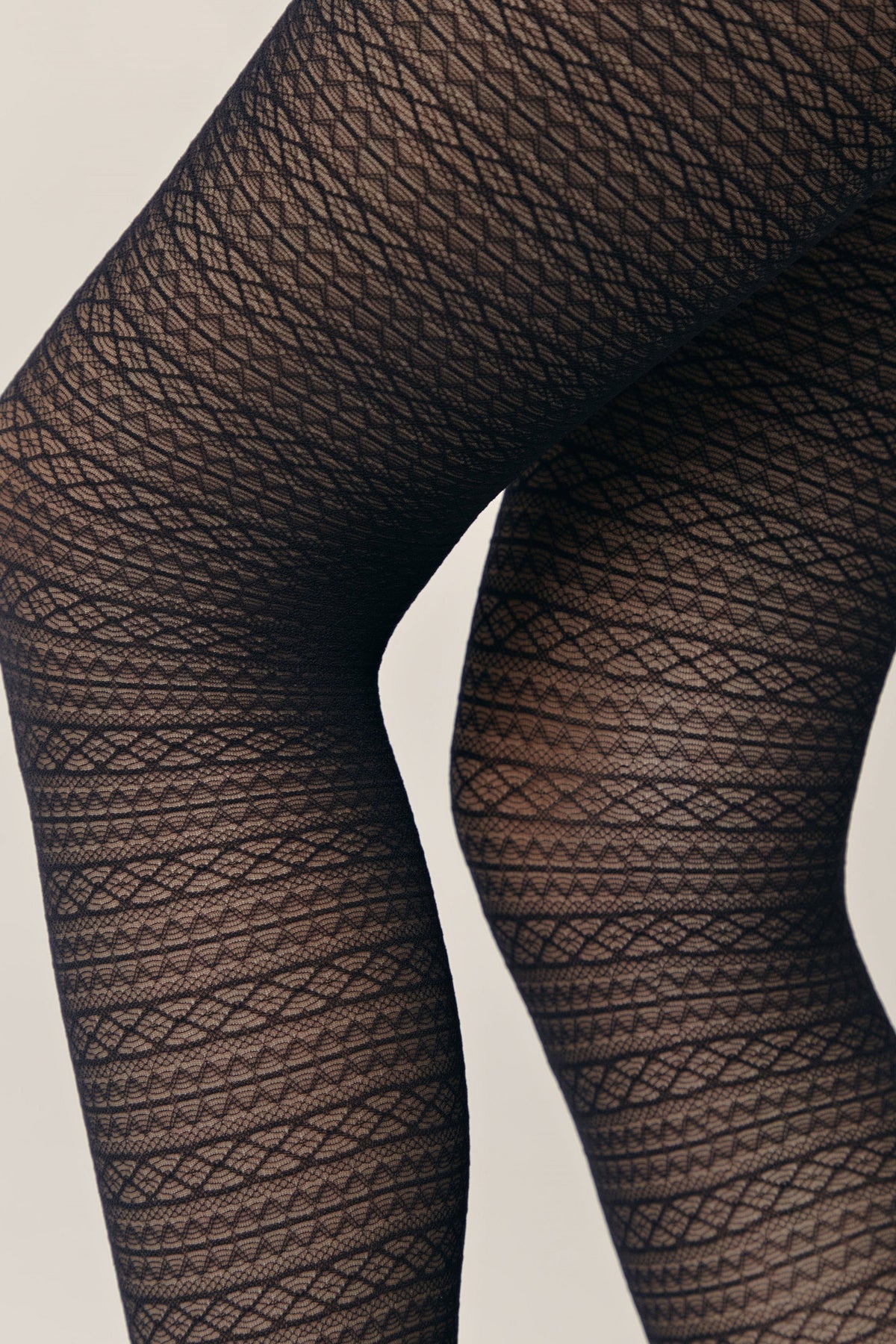 A close-up view of a person wearing black patterned tights with an intricate horizontal geometric textured knit design.