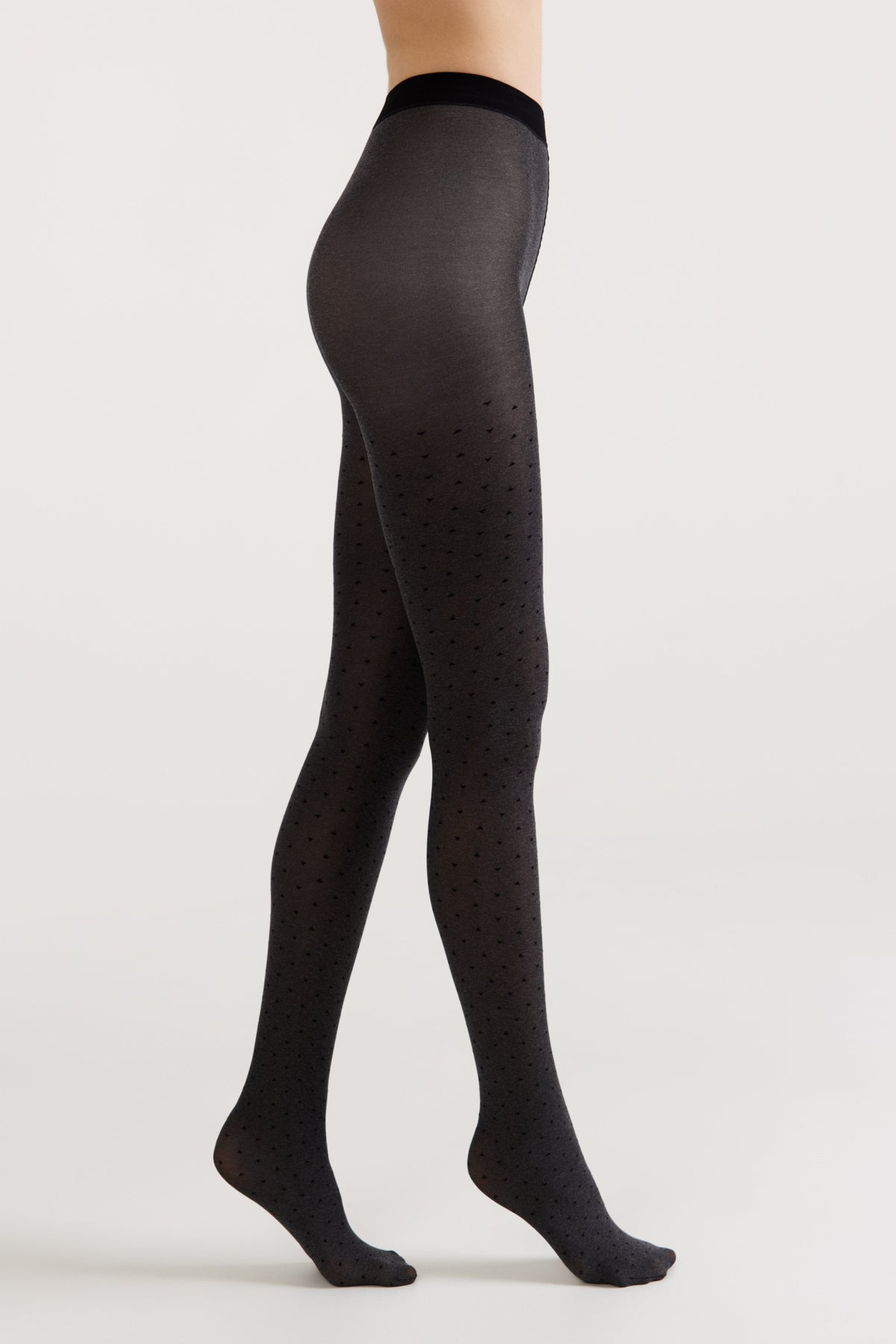 Side view of a person wearing charcoal grey tights featuring a subtle pattern of tiny, dark heart shapes against a plain white background.