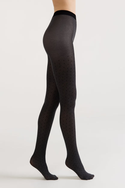 Side view of a person wearing charcoal grey tights featuring a subtle pattern of tiny, dark heart shapes against a plain white background.