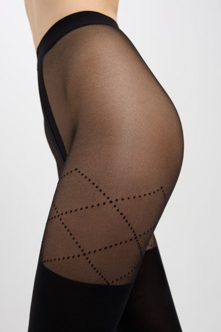 A close-up side view of a person wearing sheer black tights featuring a decorative diamond-patterned dotted design on the thigh and solid opaque black fabric extending down the leg.