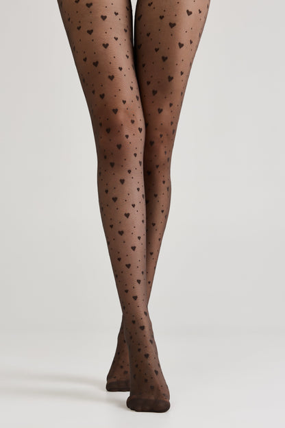Sheer black tights patterned with small dark hearts worn on a person's legs against a plain light gray background.